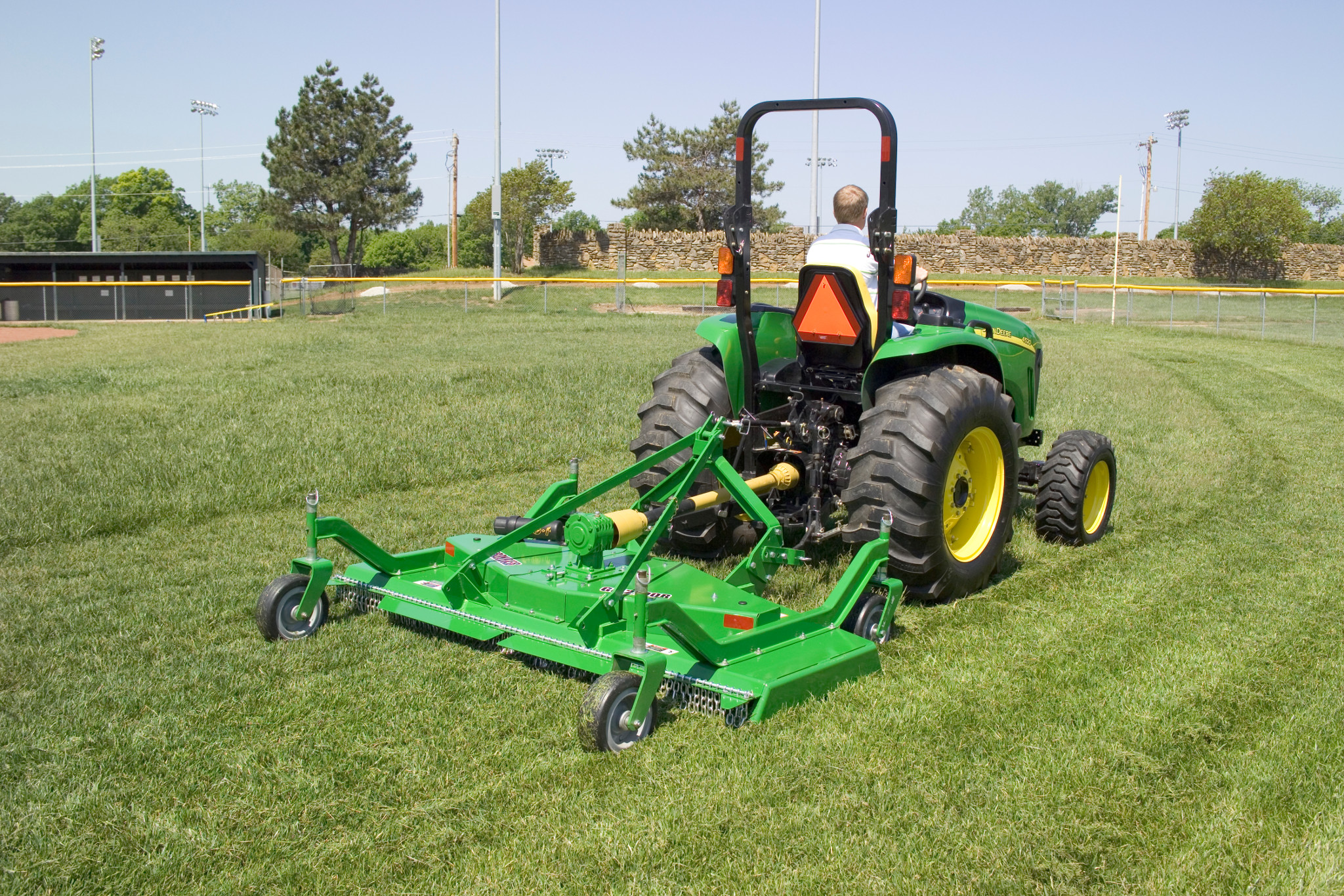 Rear right view of a John Deere tractor pulling a green GM2190R grooming mower on a sports field