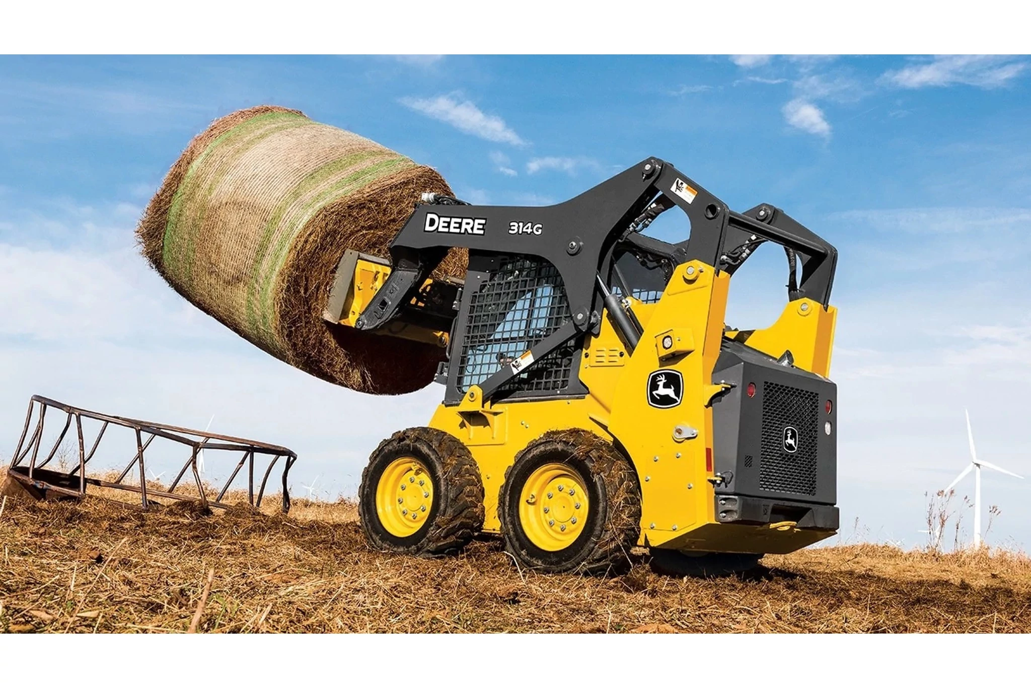Left view of 314G Skid Steer Loader with bale spear attachment carrying a round bale in a field