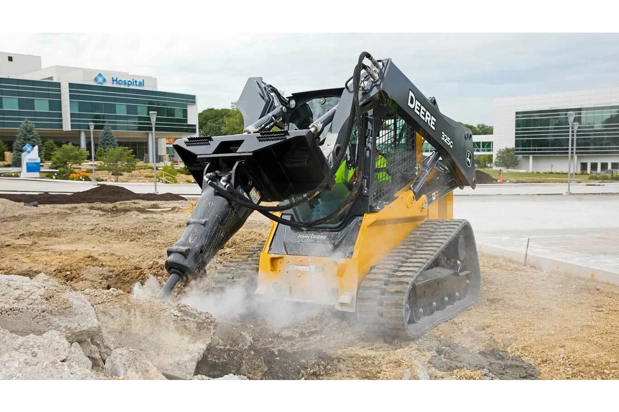 Front left view of 325G Compact Track Loader with hydraulic hammer breaking up concrete in a parking lot