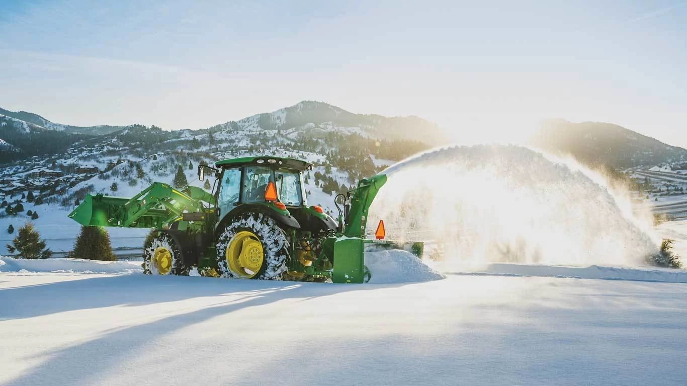 SB13 Snowblower attached to a tractor blowing snow in front of a mountain