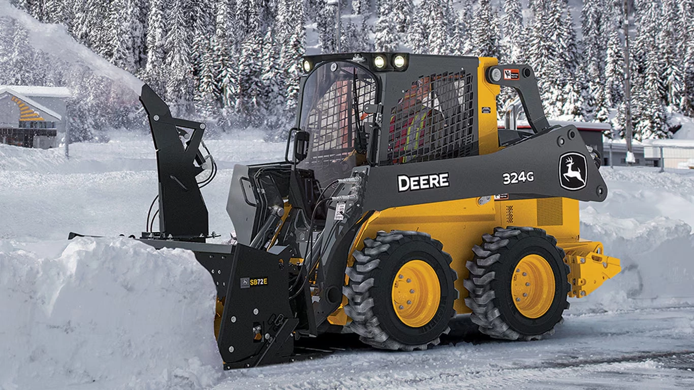 Front left view of SB72E Snow Blower on a 324G Skid Steer blowing snow off of a driveway