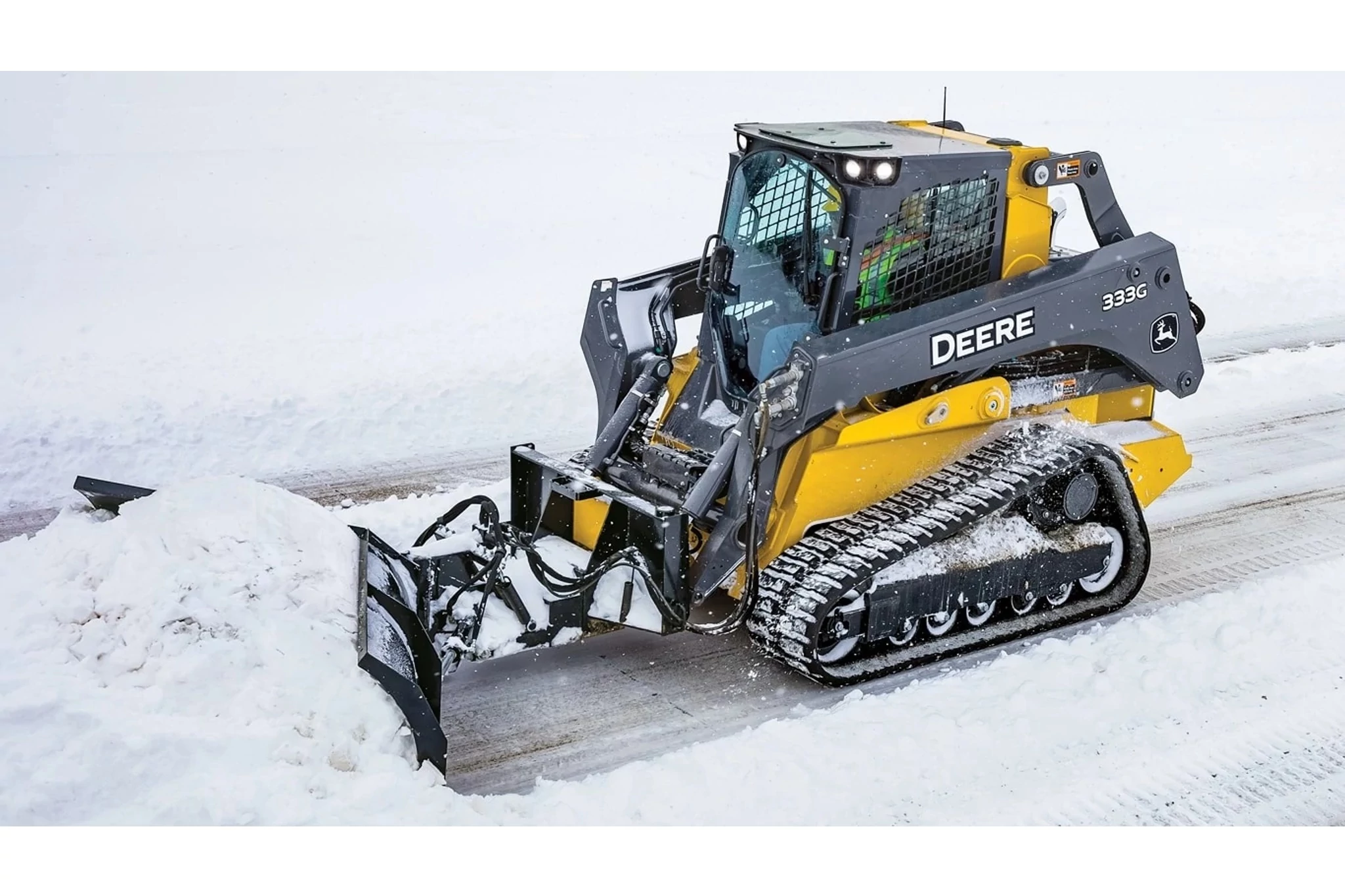 Front left view of a V-Blade on 333G Compact Track Loader pushing snow on a road